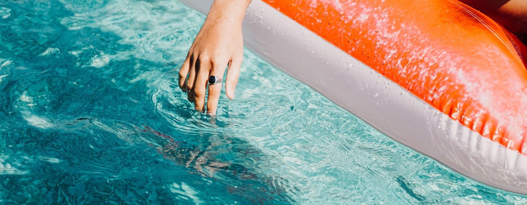 woman dangles her hand in the pool as she floats in an inflatable vessel